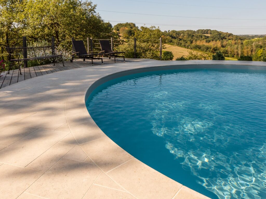 Piscina redonda com praia e bordas em calcário Alhambra: suavidade ao toque, tonalidade quente e elegância mediterrânica para espaços exteriores com charme intemporal