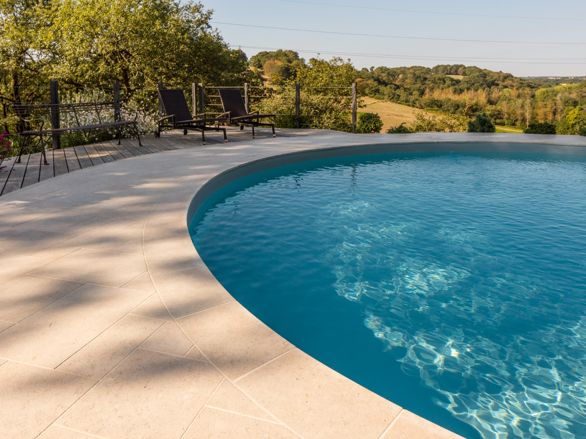 Piscina redonda com praia e bordas em calcário Alhambra: suavidade ao toque, tonalidade quente e elegância mediterrânica para espaços exteriores com charme intemporal